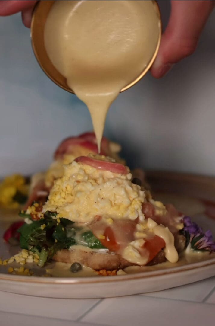 Hollandaise sauce being poured over eggs benedict.